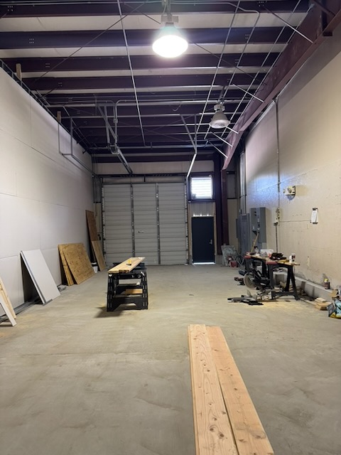 Bay 2 interior looking toward the overhead door and personnel door, with framing lumber staged on the floor